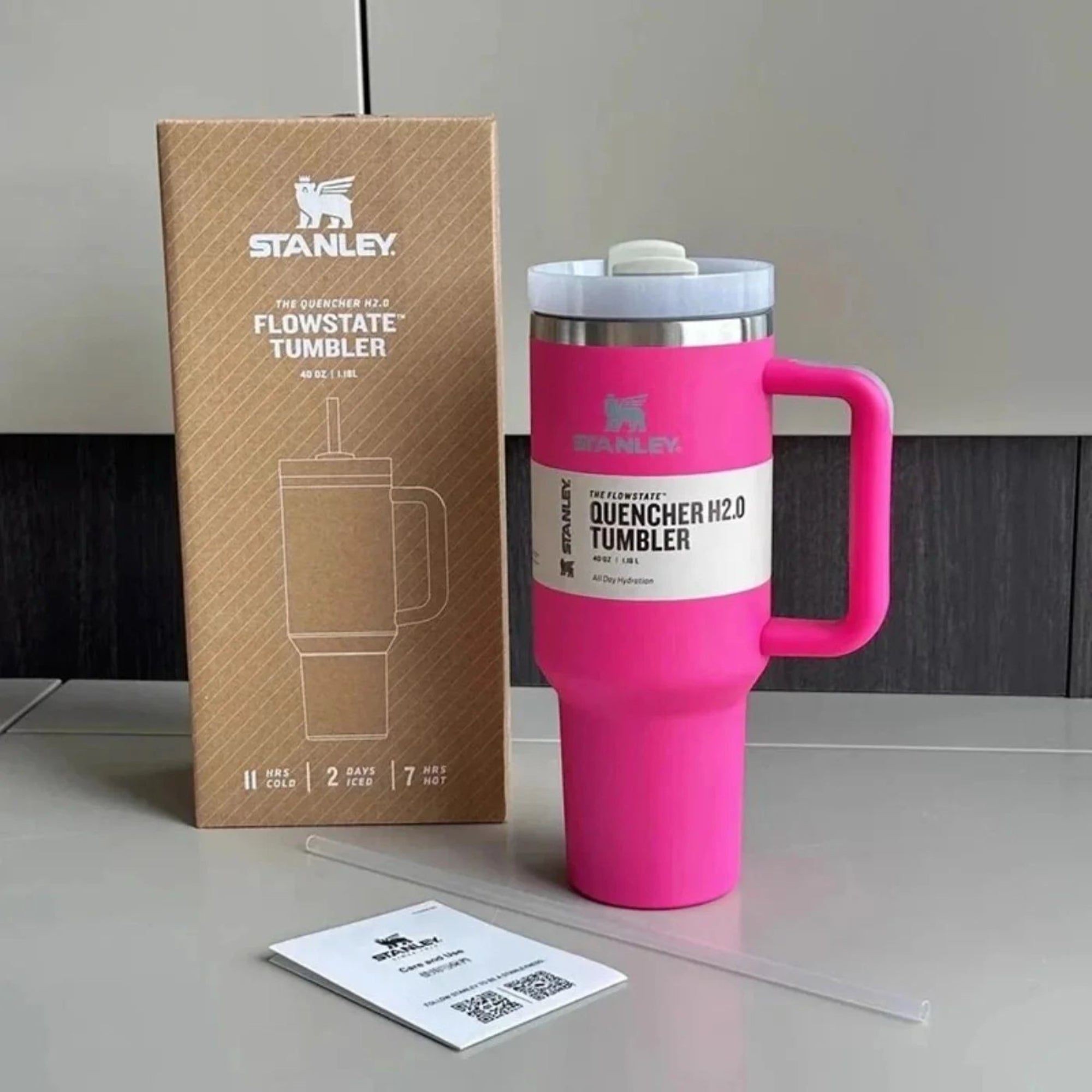 Pink Stanley tumbler with handle next to its packaging on a neutral background