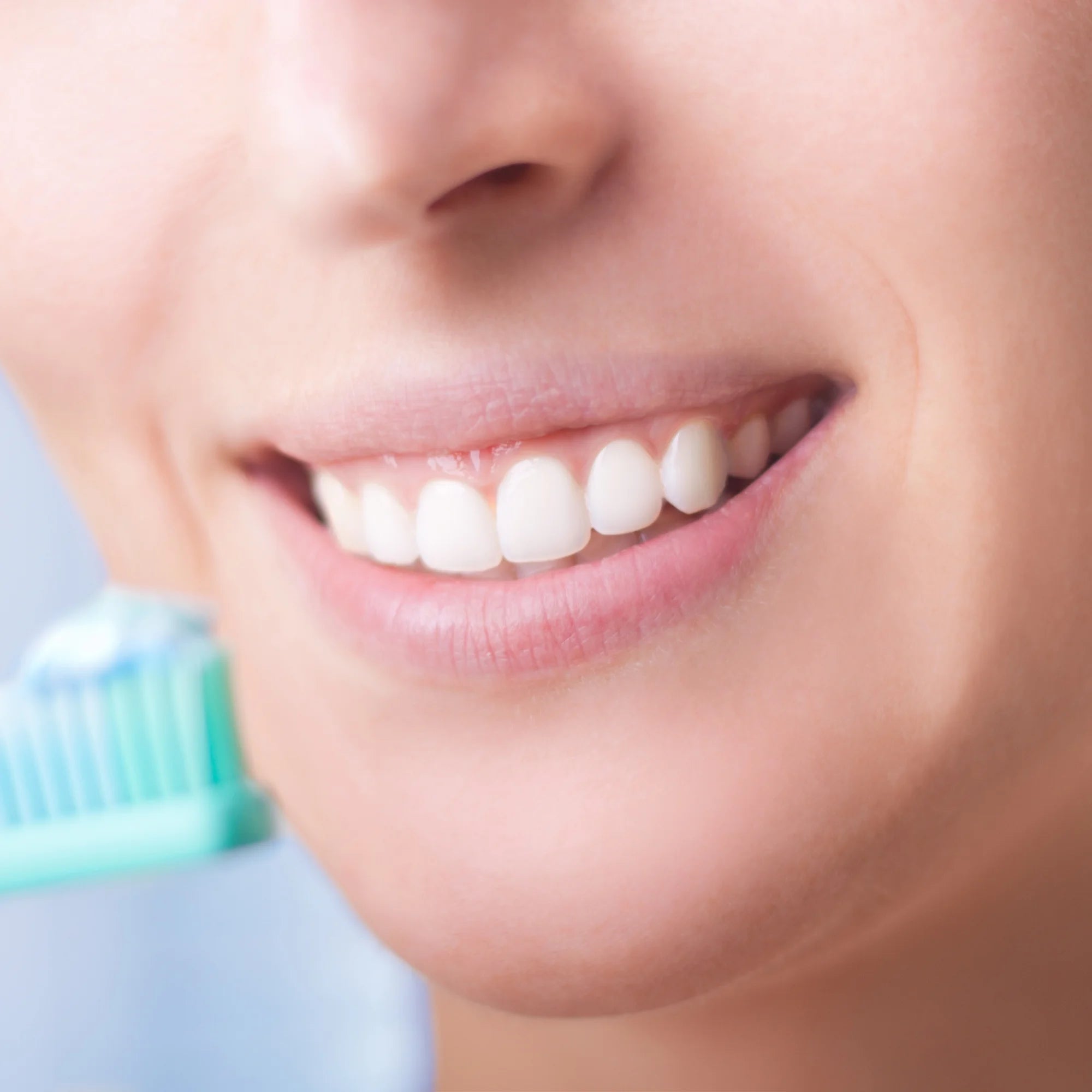 Close-up of a person's smiling mouth with a toothbrush in the background