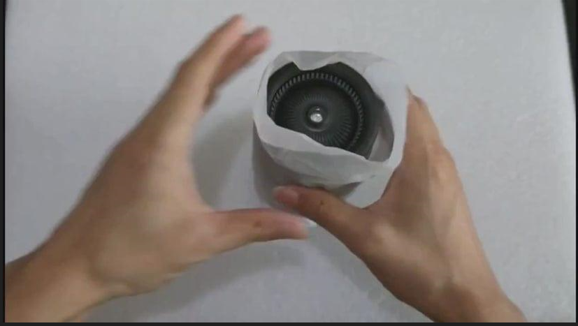 Person holding a cylindrical electronic device with a white exterior and black interior on a plain background